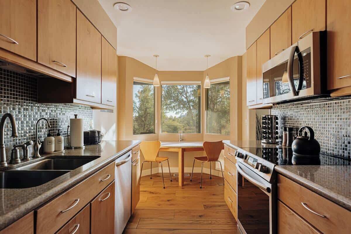 A modern kitchen with wooden cabinets, a large window, and a dining area.