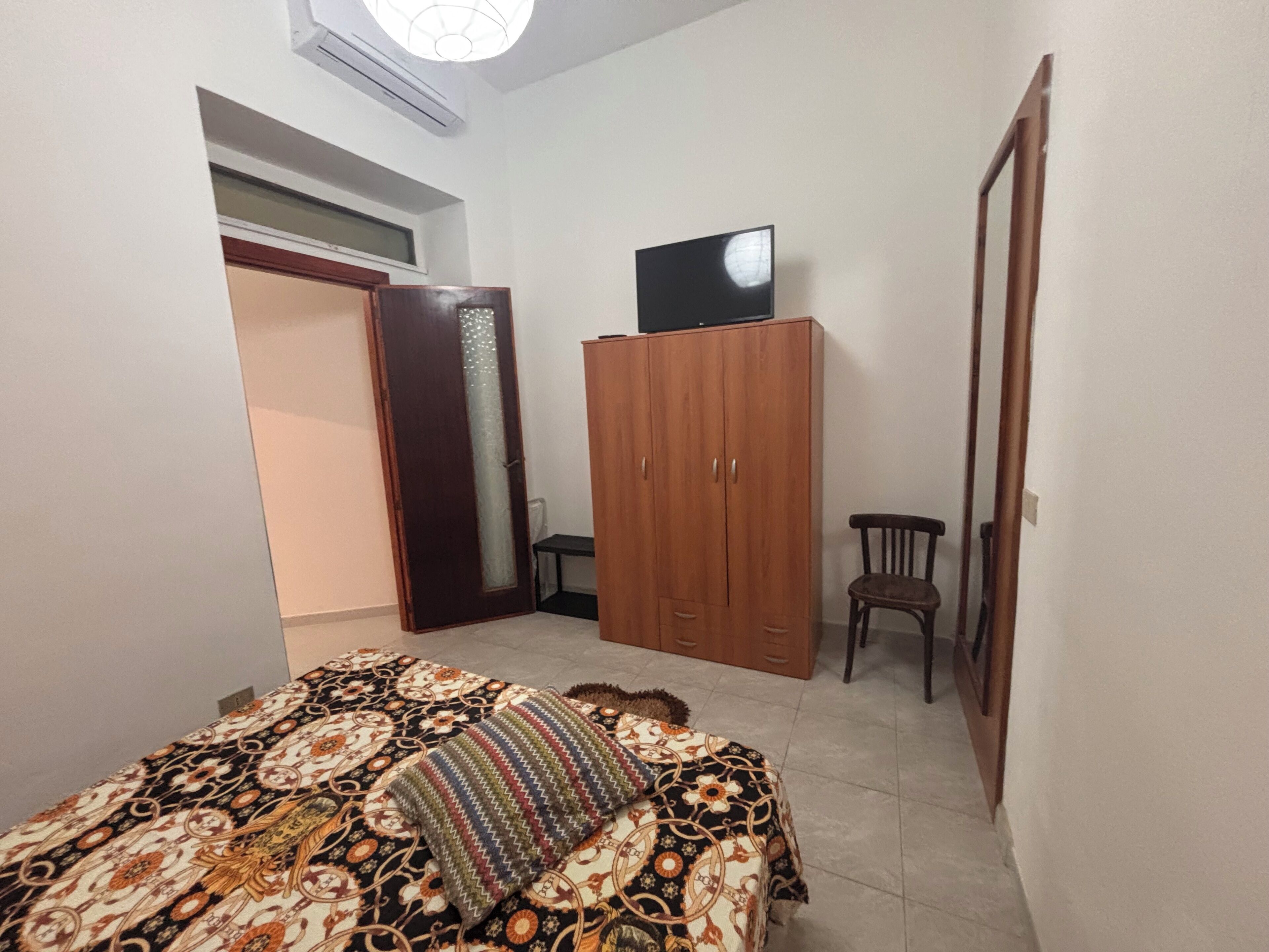 A bedroom with a bed, wardrobe, TV, and a chair.