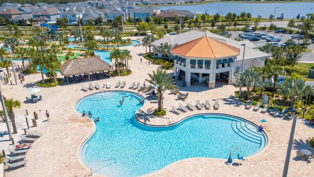 A resort with a large, curved swimming pool surrounded by lounge chairs and palm trees.