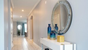 A hallway with a white console table, blue vases, and a mirror with a diamond frame.