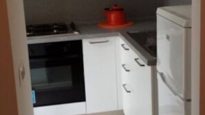 Une cuisine avec des armoires blanches, un fourneau, une casserole rouge et un réfrigérateur.
