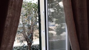 Une vue depuis un balcon avec une rambarde en métal, un arbre et un bâtiment en arrière-plan.