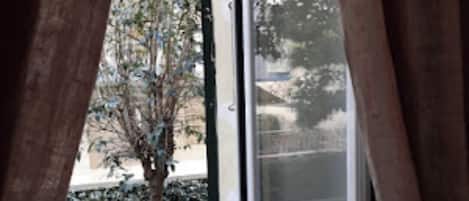 Une vue depuis un balcon avec une rambarde en métal, un arbre et un bâtiment en arrière-plan.