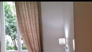 Une chambre à coucher avec un lit, une fenêtre avec des rideaux, un radiateur et un luminaire fixé au mur.