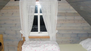 Ein Einzelbett mit Holzrahmen und weißer Bettwäsche, ein Fenster mit weißen Vorhängen und ein Holzboden.