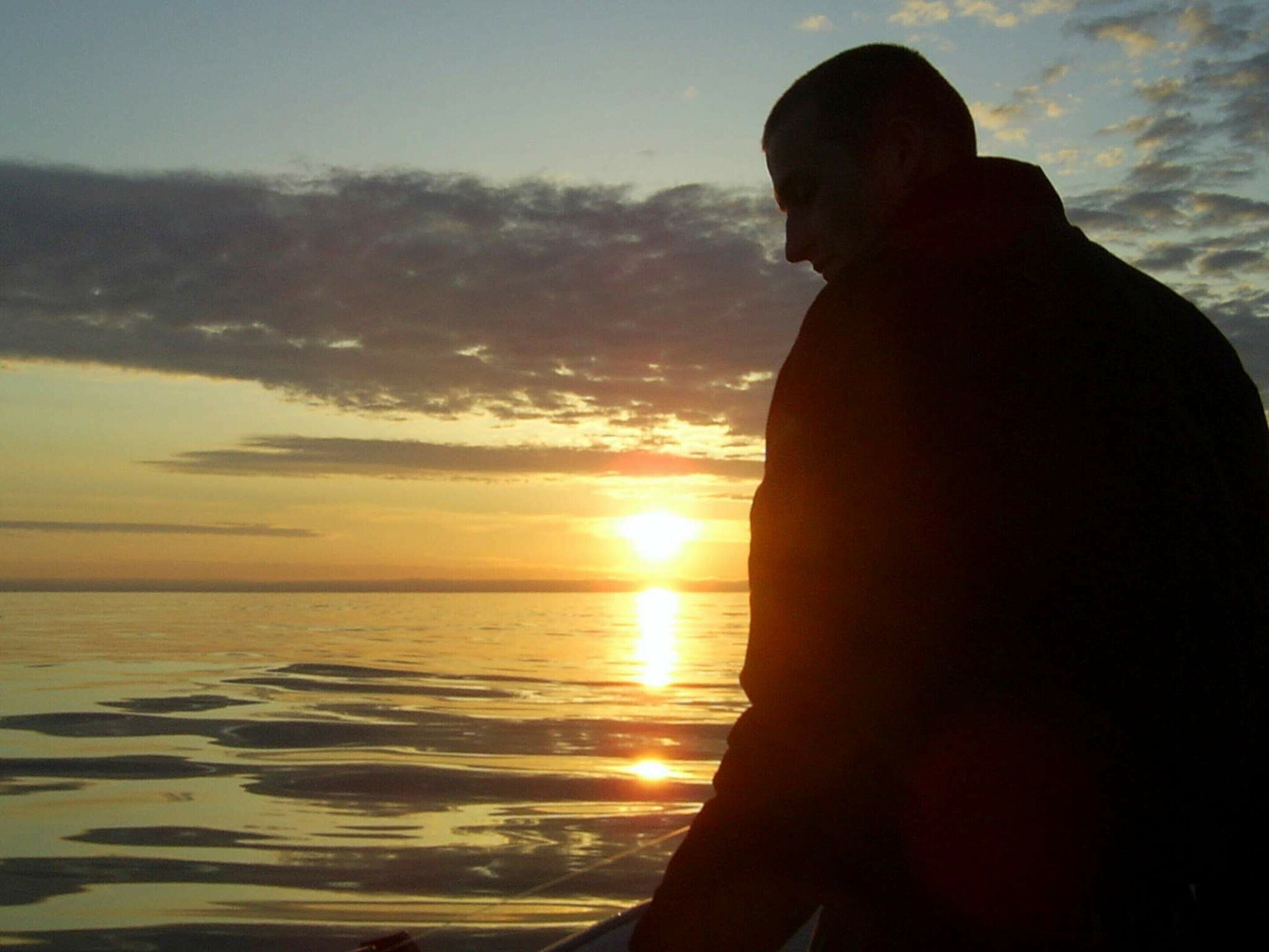 A person sitting by the water during sunset.