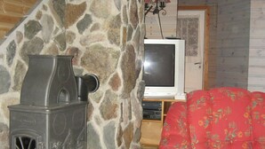 Eine Steinsäule, ein alter Herd, ein Fernseher und ein floral gemustertes Sofa in einem gemütlichen Raum.