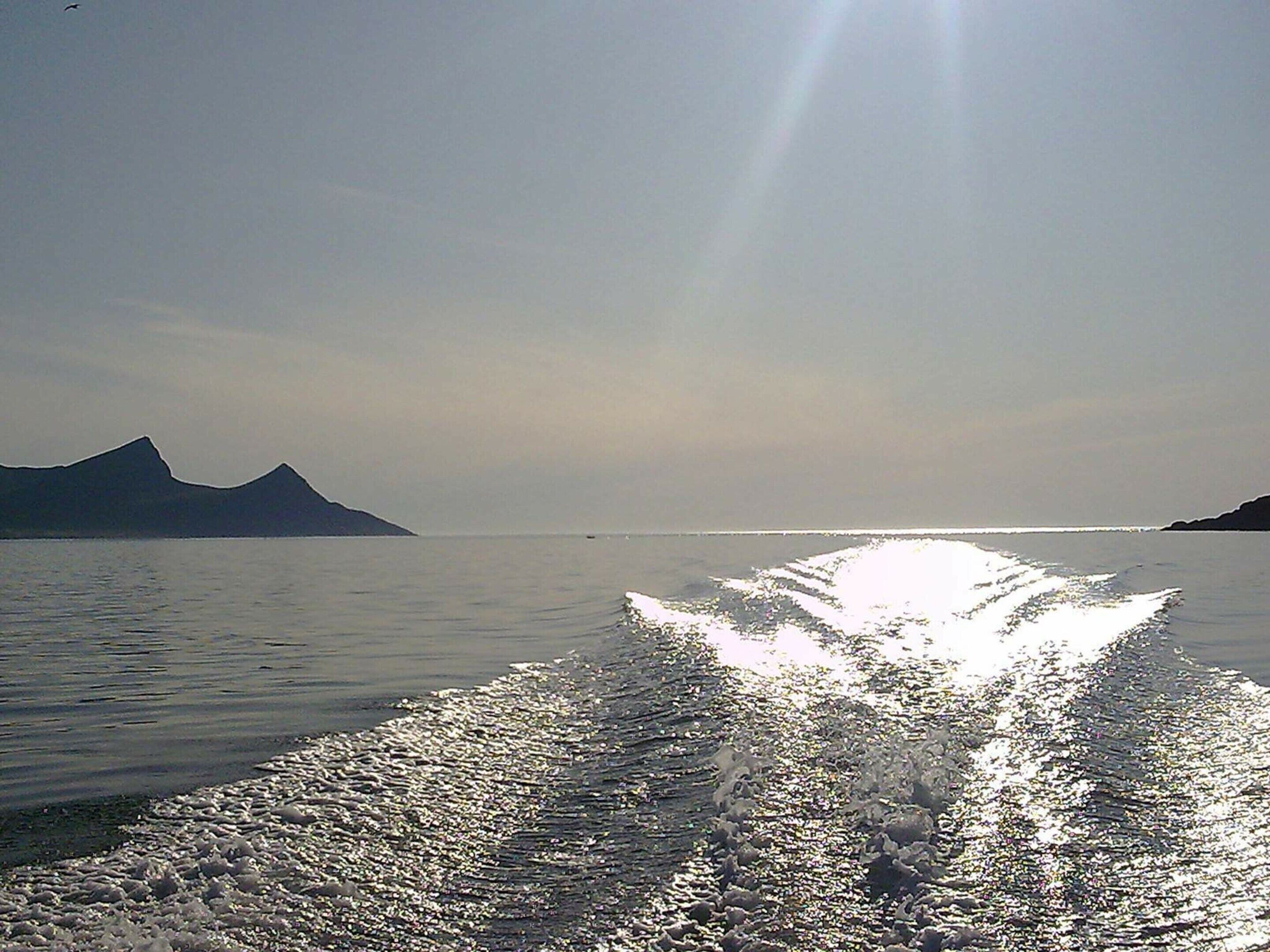 A boat's wake on calm water with mountains in the background.