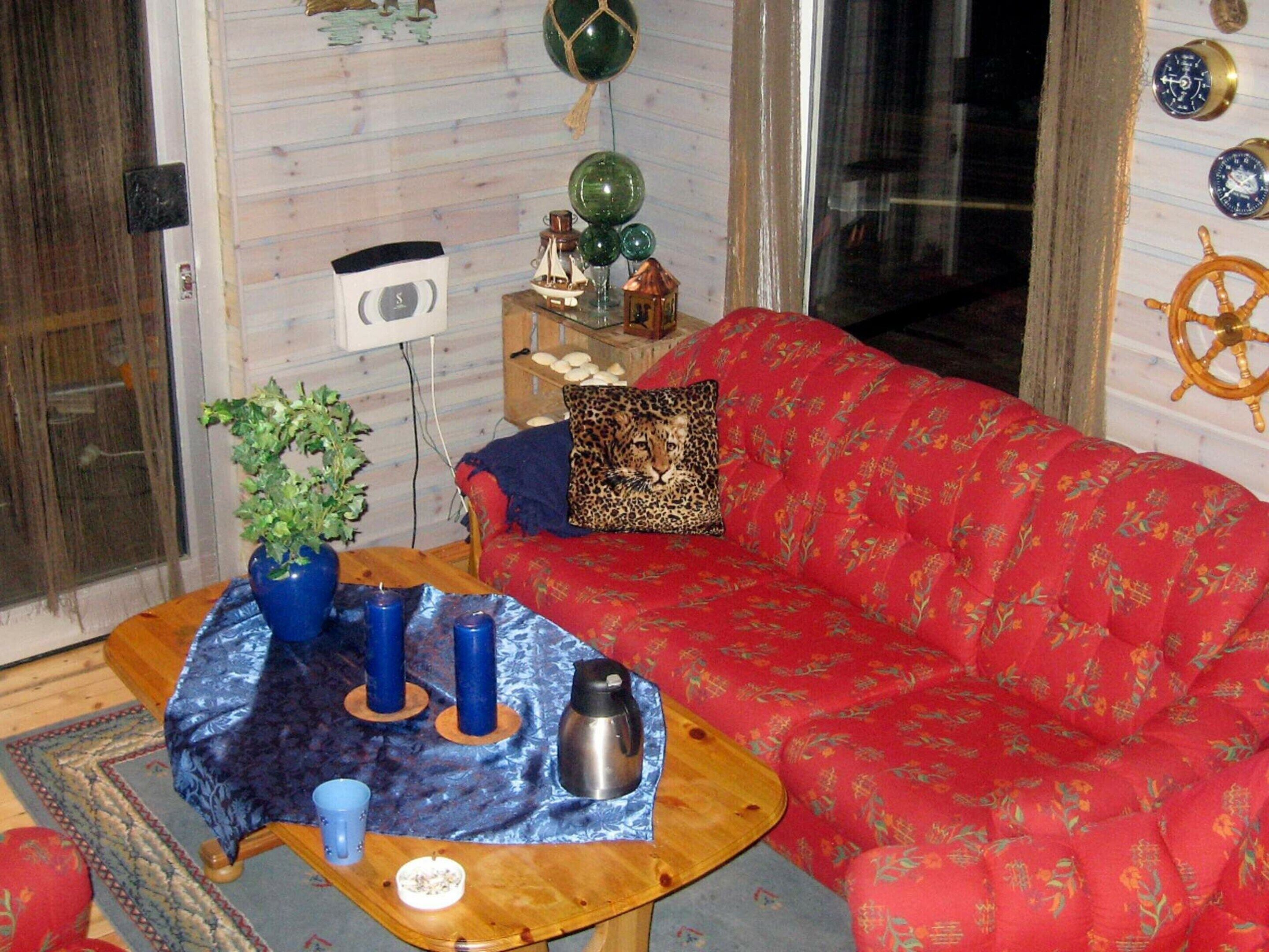 Una sala de estar acogedora con un sofá rojo, una mesa de centro de madera y un mantel azul estampado. Hay un cojín de estampado de leopardo en el sofá y una planta en maceta sobre la mesa.