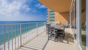 A balcony with a table and chairs, overlooking a beach and ocean.