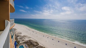 A beach view from a balcony with a pool and sun loungers.