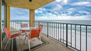 A balcony with a table and chairs, overlooking a beach and the ocean.