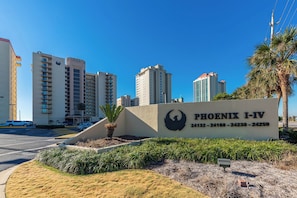 Señal de Phoenix I-IV con logotipo de ave, rodeada por un área ajardinada con palmeras y un estacionamiento.
