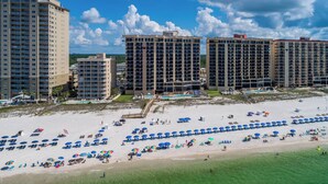 A beachfront hotel with multiple high-rise buildings, a sandy beach with numerous umbrellas, and a clear blue sky.