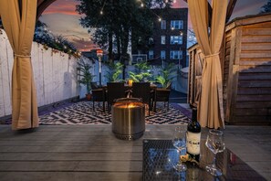 Un patio exterior con un brasero, una mesa de comedor, sillas y una botella de vino.