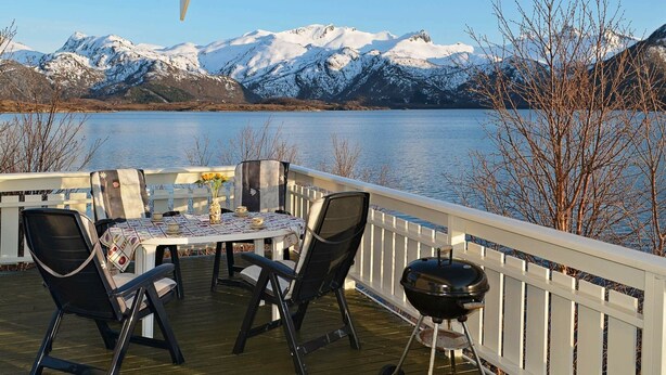 A deck with a table and chairs overlooking a lake with snow-capped mountains in the background. - 5 Person Holiday Home in Laukvik-by Traum (Vagan)