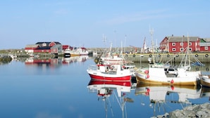 A harbor with several boats docked, a red building, and calm water reflecting the structures. - 5 Person Holiday Home in Laukvik-by Traum (Vagan)