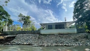 A river with rocks and a building with a metal roof in the background.