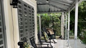 A covered outdoor seating area with rows of black metal chairs and white cushioned seats, a tiled floor, and a metal roof.