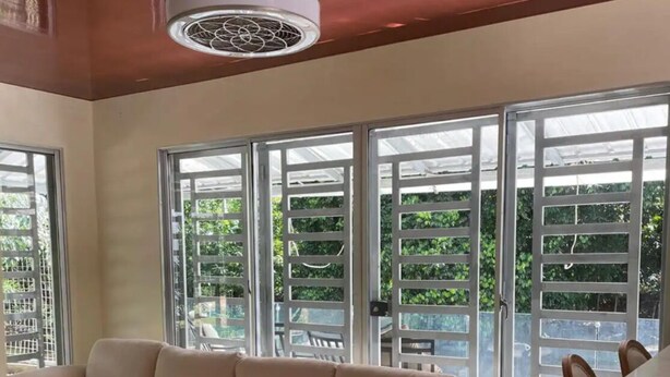 A spacious living room with a beige sectional sofa, a dining table with chairs, and large windows with a view of greenery.