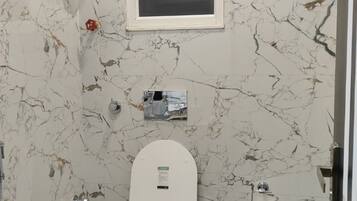 A bathroom with a toilet, a shower, and a wall-mounted air conditioning unit.