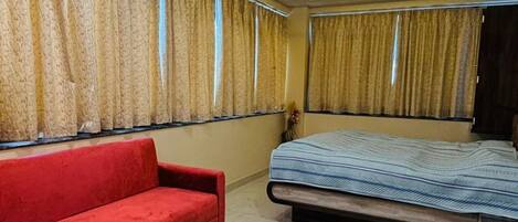 A modern bedroom with a red sofa, a bed with a blue bedspread, a small table with a plant, and a ceiling fan.