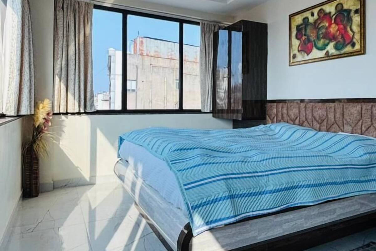 A bedroom with a large bed, a ceiling fan, a window with curtains, and a painting on the wall.