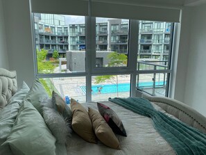 Une chambre avec une grande fenêtre donnant sur une piscine et des bâtiments modernes.