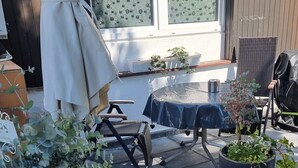 A patio area with a table, chairs, potted plants, and a grill.