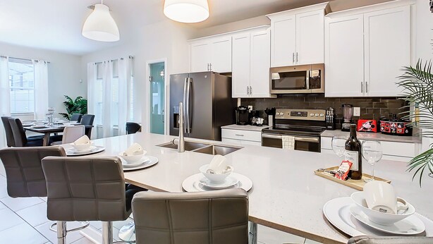 A modern kitchen with white cabinets, stainless steel appliances, and a dining area with a long table and chairs. - 5BR Townhouse Near Disney Pool (Kissimmee)