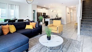 A modern living room with a dark sofa, a round coffee table, and a dining area with a table and chairs. - 5BR Townhouse Near Disney Pool (Kissimmee)