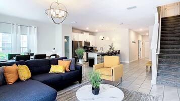 A modern living room with a dark sofa, a round coffee table, and a dining area with a table and chairs.