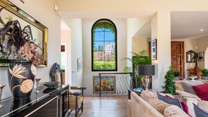 A spacious living room with a large window, a black console table, a vintage armchair, a sofa, and a radiator. - Luxury Villa - Sleeps up to 8 & Infinity Pool (Estepona)