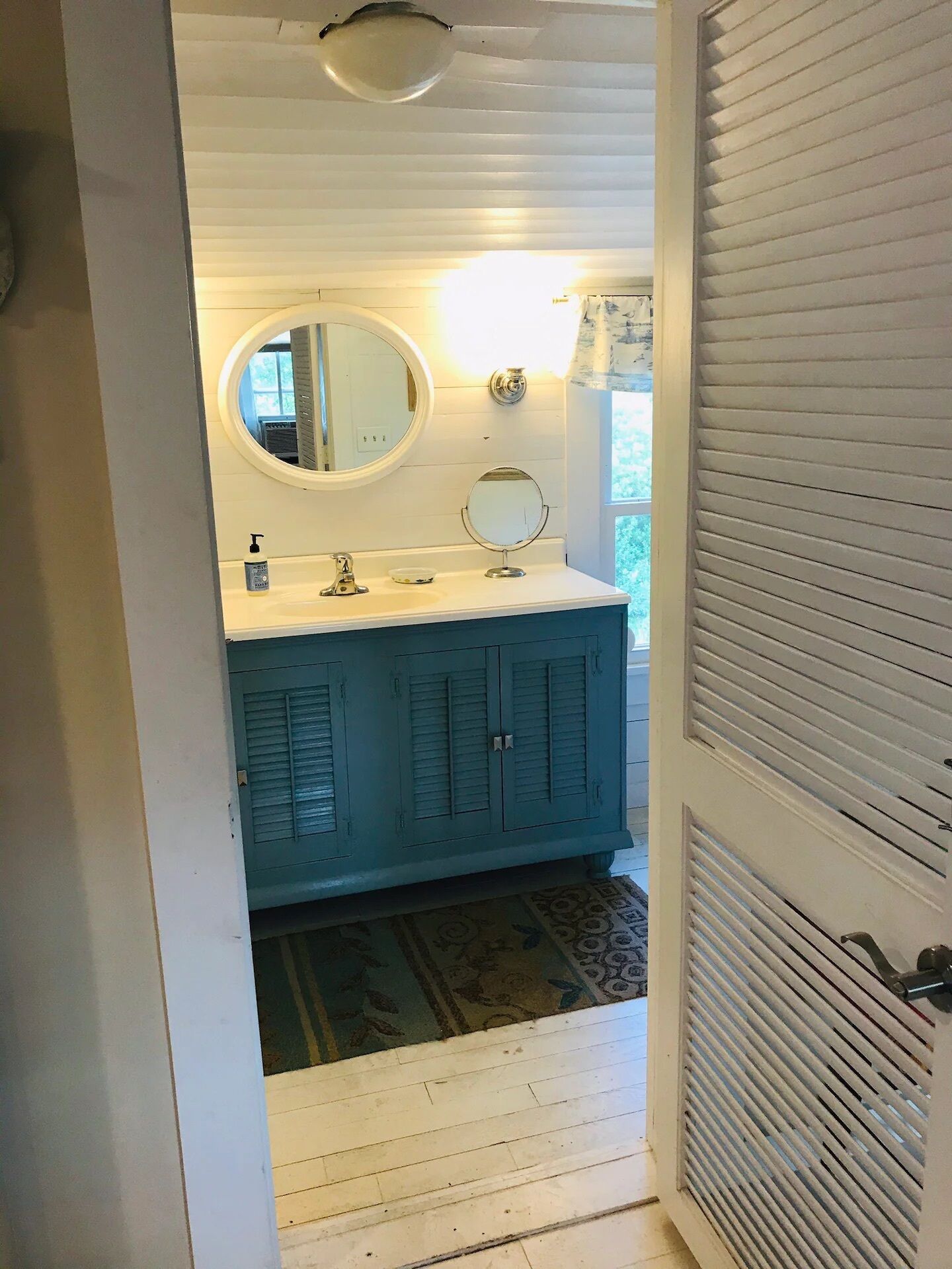 A bathroom with a white vanity, a round mirror, and a blue cabinet.