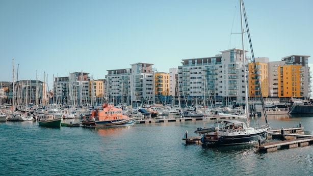 A marina with various boats docked, surrounded by modern multi-story buildings.