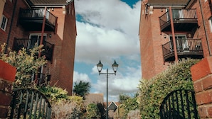 A pathway leading to a residential building with brick walls, balconies, and a street lamp.