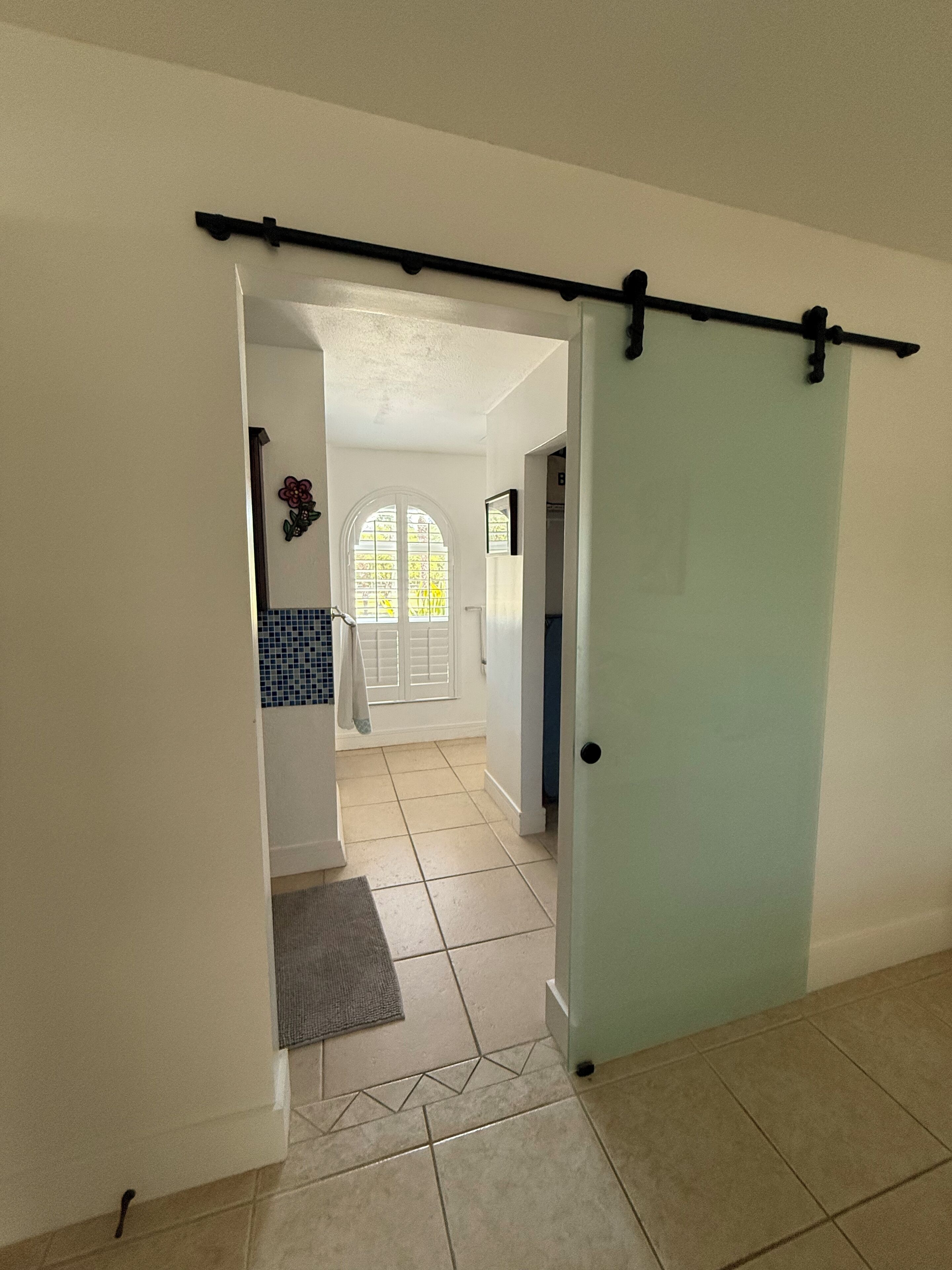 A hallway with a sliding door, a tiled floor, and a view into a room with a window and a door.