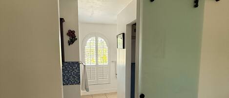 A hallway with a sliding door, a tiled floor, and a view into a room with a window and a door.