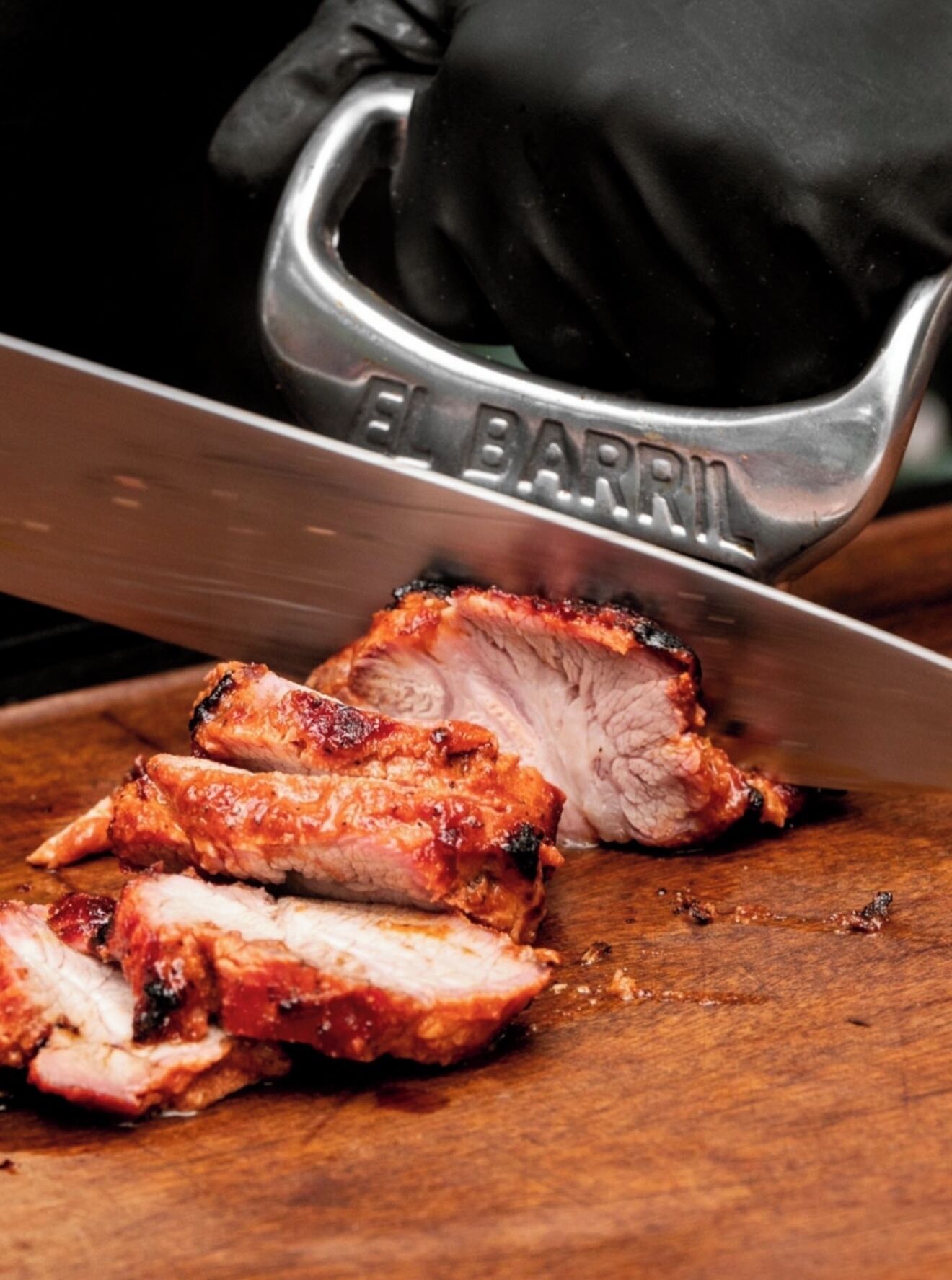 A person slicing meat on a wooden cutting board.