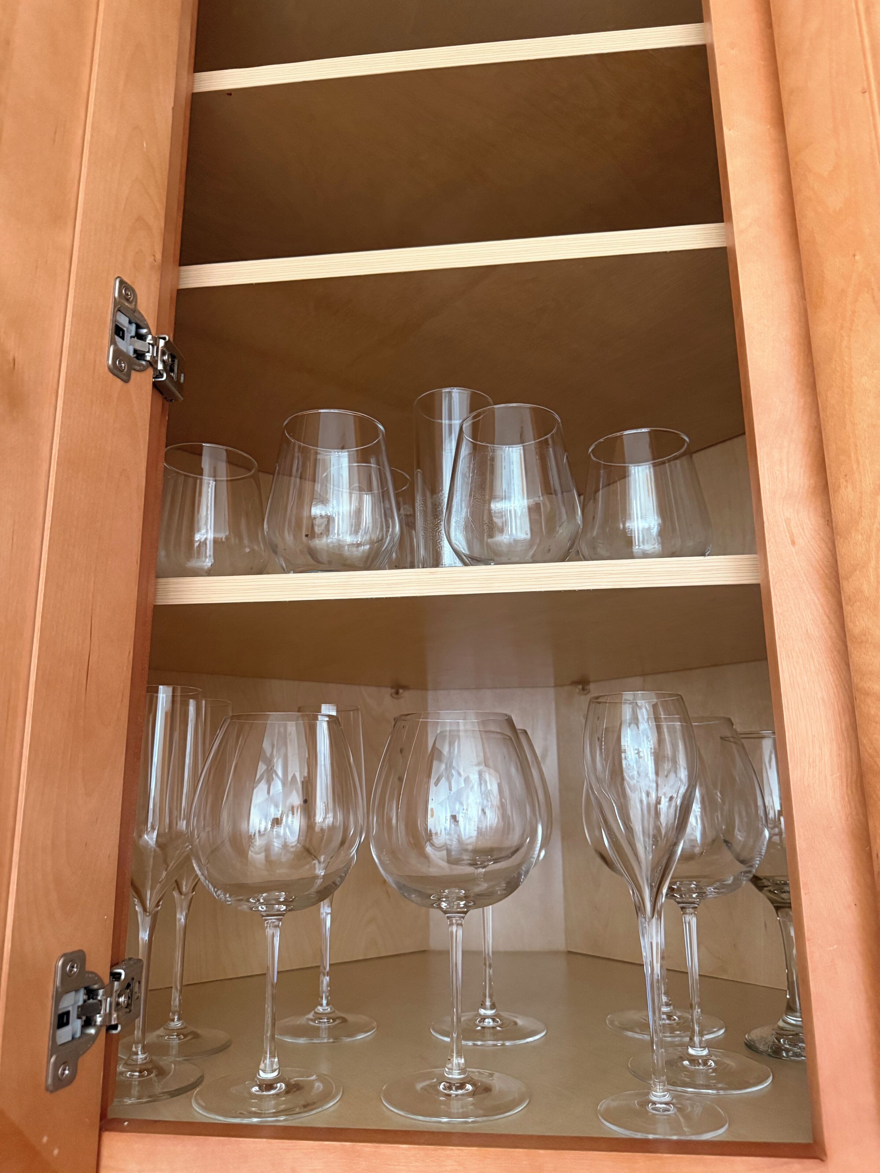 A wooden cabinet with multiple shelves, each holding clear glassware.