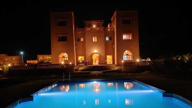 A large building with a swimming pool at night, illuminated by warm lights. - Hotel Kasbah Riad Amnir (M'Hamid El Ghizlane)