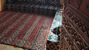A room with a patterned sofa set, a large woven rug, and a wooden carved cabinet. - Hotel Kasbah Riad Amnir (M'Hamid El Ghizlane)