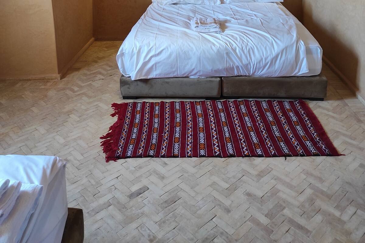 A bedroom with a large bed, wooden ceiling, wall-mounted air conditioning, and two bedside lamps.