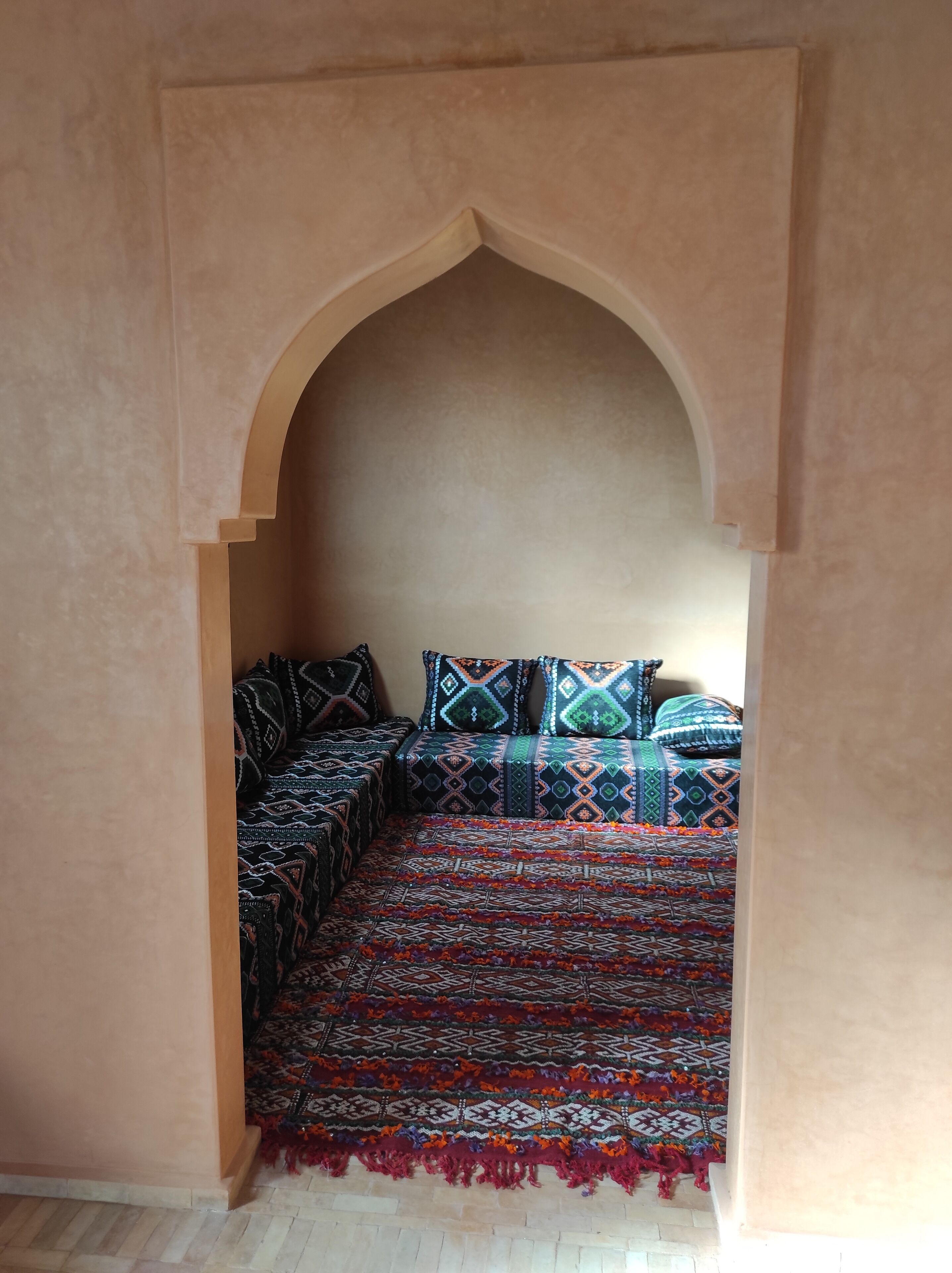 A cozy room with a low arched doorway, a patterned bedspread, and a matching rug.