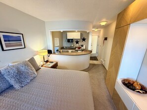 Ein Hotelzimmer mit einem großen Bett, einem kleinen Schreibtisch, einer Küchenzeile und einem durch eine offene Tür einsehbaren Badezimmer.