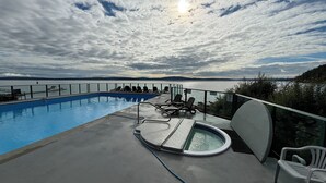 A pool area with a view of the sea, lounge chairs, and a hot tub. - Oceanfront Escape - Studio with kitchenette  (Ladysmith)