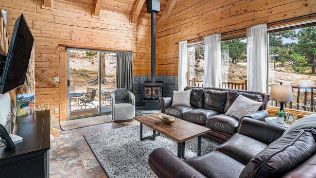 Un intérieur de chalet chaleureux avec une cheminée, des canapés en cuir et une grande fenêtre donnant sur le paysage extérieur.