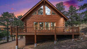 Une cabane en rondins dotée d’un balcon, entourée d’arbres et sous un ciel dégagé.