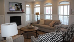 A living room with a fireplace, a television mounted above it, and a sofa with patterned cushions.