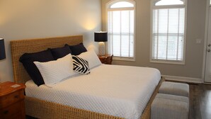 A bedroom with a large bed, two bedside tables, and a window with blinds.
